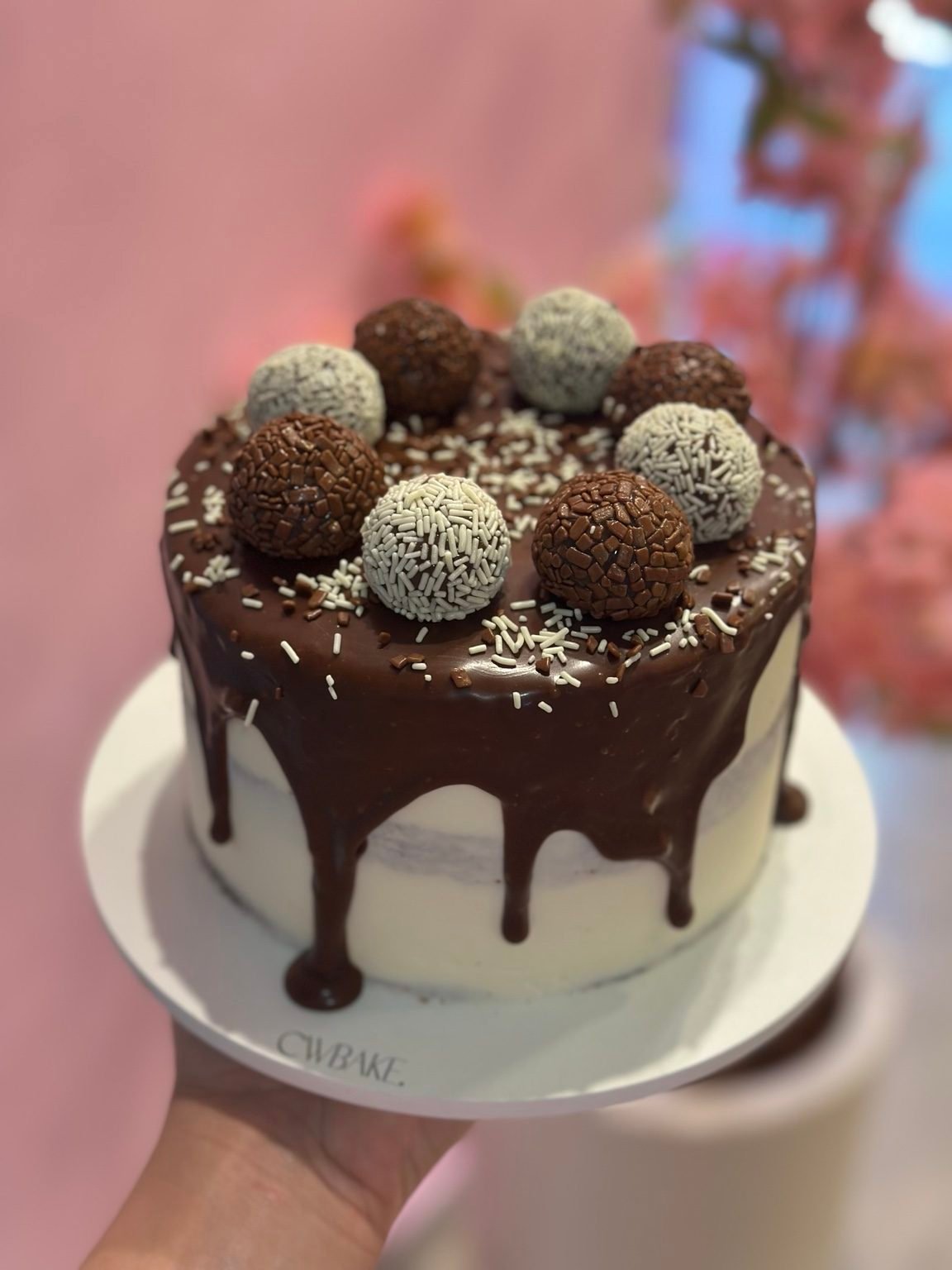 Bolo com drip de chocolate e brigadeiros brancos e escuros no topo