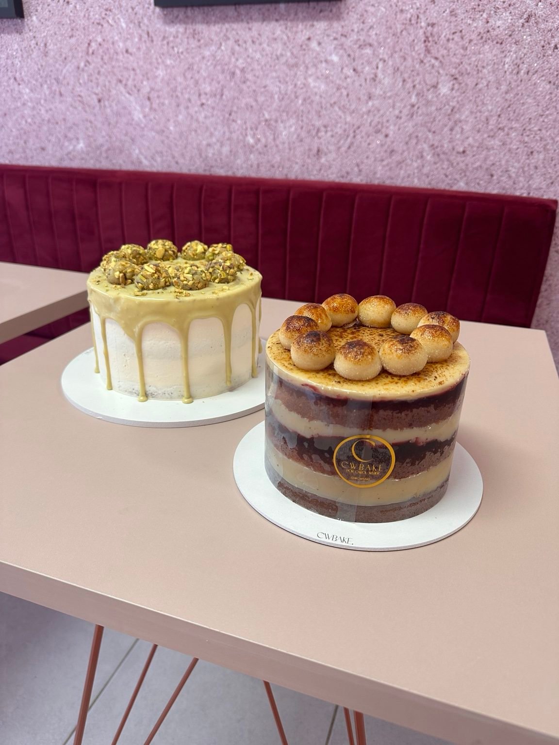 Dois bolos: um com drip branco e pistache no topo e outro naked com brigadeiros de brulée