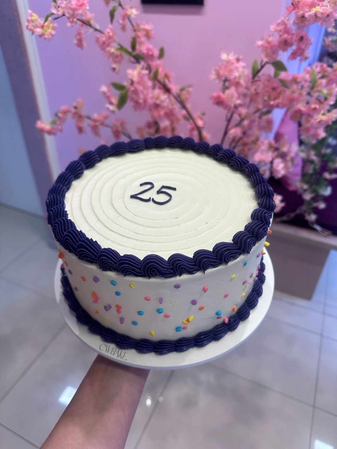 Bolo branco com confeitos coloridos, bordas azuis e o número 25 no topo