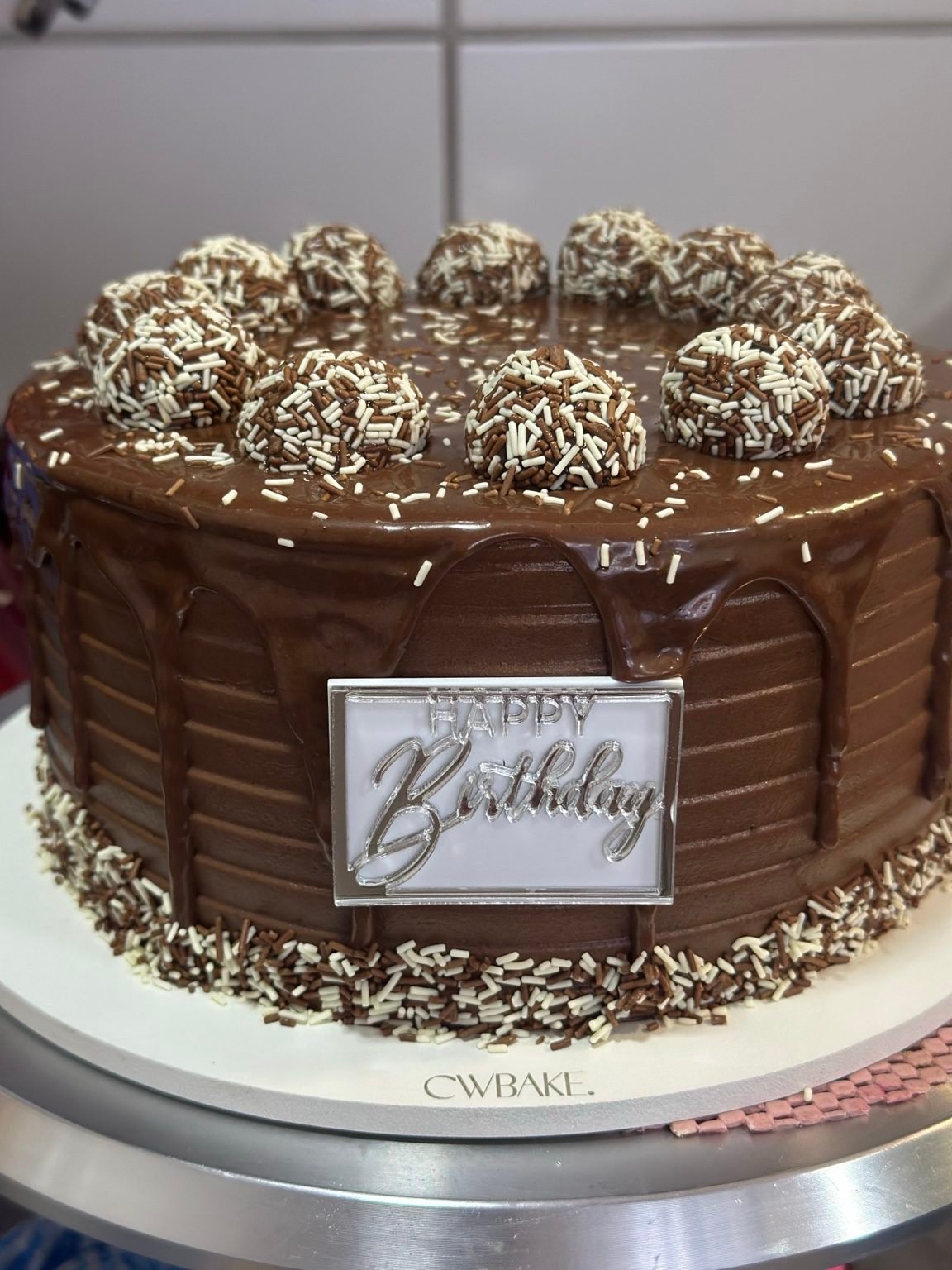 Bolo coberto de chocolate com brigadeiros e placa “Happy Birthday”